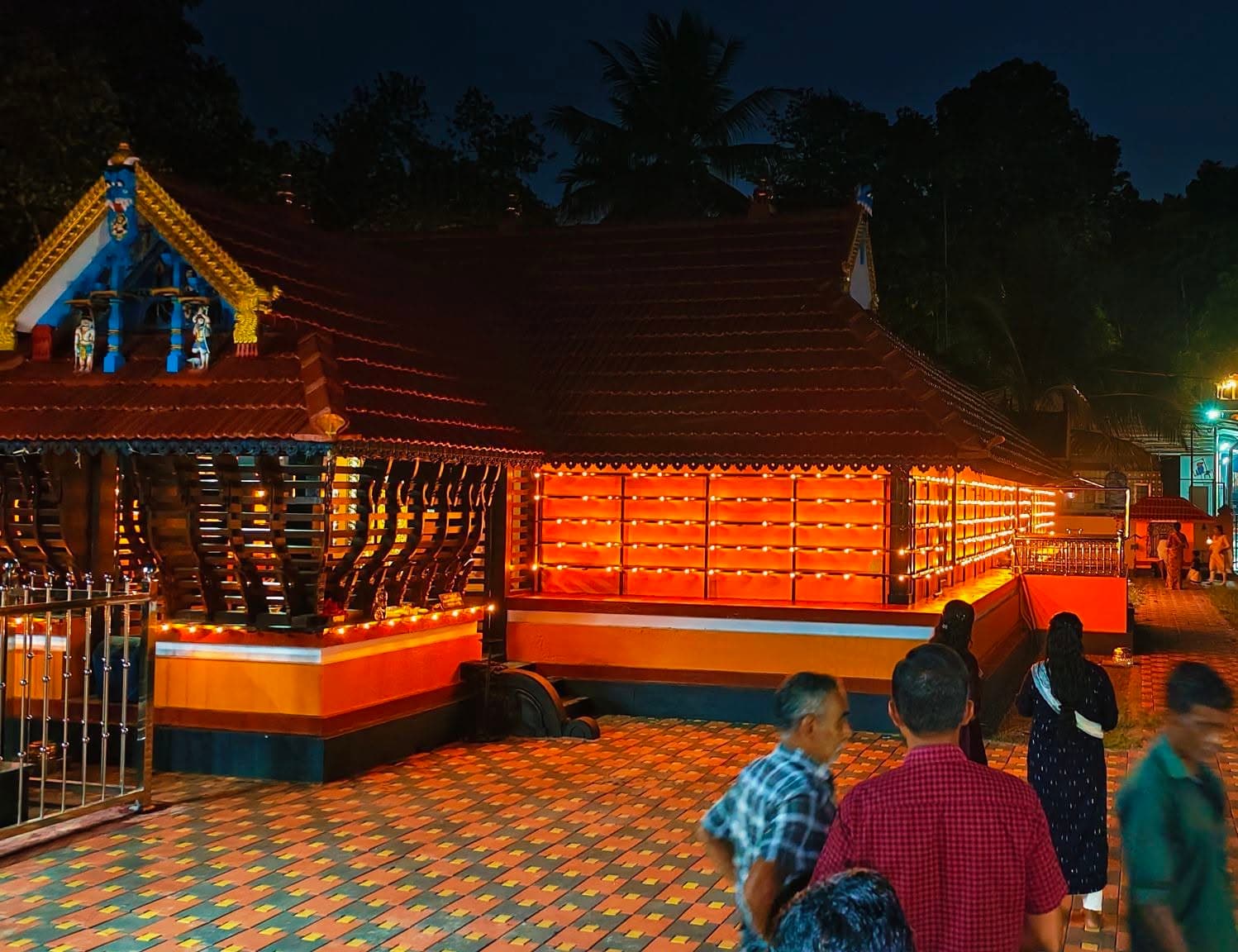 Annapoorneswari Devi Temple at dusk — the tiled-roof shrine lit with rows of oil lamps as devotees gather in the brick courtyard